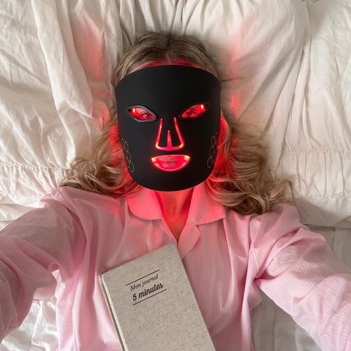 Woman wearing Lumé red light therapy face mask with red light glow visible through mask